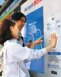 젊은이들이 버스정류장에 설치된 '박카스 셀프 스캐너'에서 손바닥 모양의 센서에 손을 갖다대고 '방전지수'를 측정해 보고 있다.   동아제약 제공